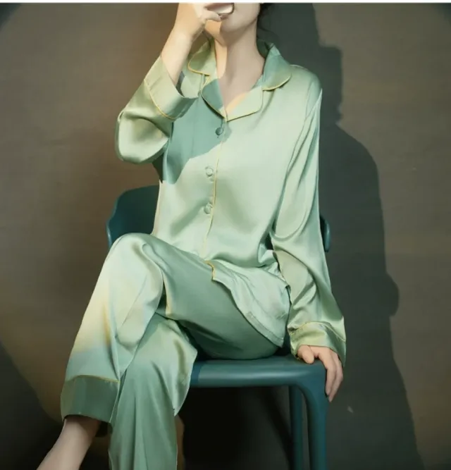 Woman seated wearing the sage silk pajama set with gold piping